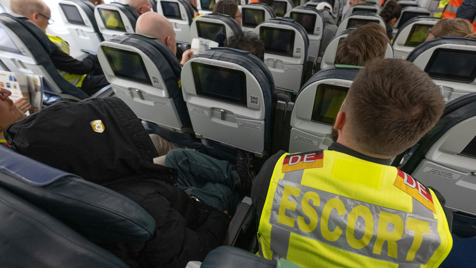 Ein Beamter der Bundespolizei sitzt an Bord eines Abschiebefluges neben einem Mann (l), der abgeschoben wird.