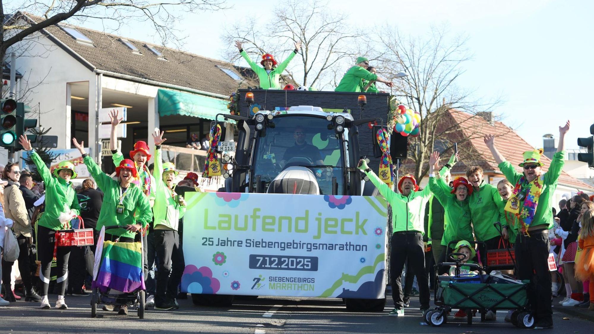Ein Traktor mit einem Schild und dem Schriftzug "Laufend jeck", links und rechts daneben Menschen in grüner Kleidung.