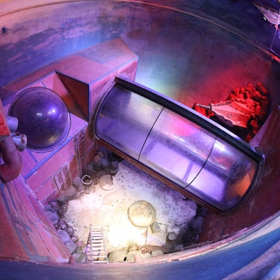 Blick in ein ehemaliges Riesenaquarium, in dem kein Wasser mehr ist. Durch das Becken verläuft eine Glasröhre.