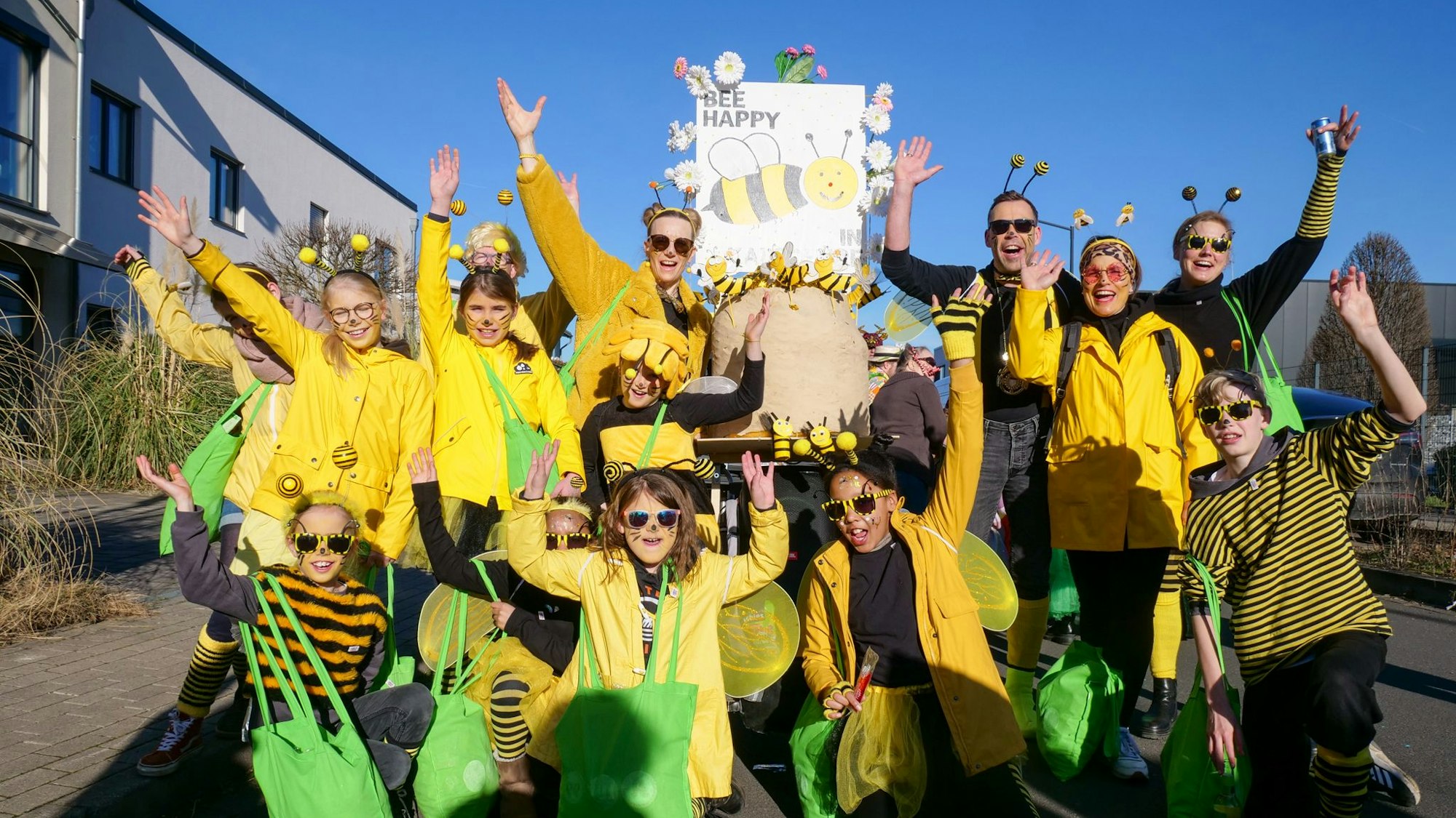 Das Foto zeigt eine große Gruppe in Bienenkostümen und einem Plakat, auf dem „Bee happy“ steht.