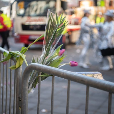 Im Rosenmontagszug in Euskirchen sind Tulpen-Sträußchen in ein Absperrgitter gesteckt. Im Hintergrund rollt ein Karnevalswagen an, verkleidete Jecke stehen auf der Straße.