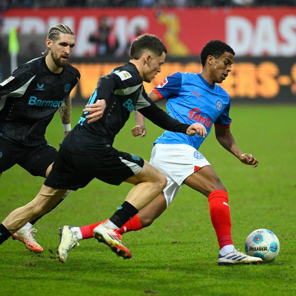 Kiels Andu Kelati (r) setzt sich gegen Leverkusens Robert Andrich (l) und Florian Wirtz durch.