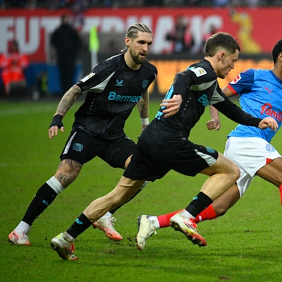 Kiels Andu Kelati (r) setzt sich gegen Leverkusens Robert Andrich (l) und Florian Wirtz durch.