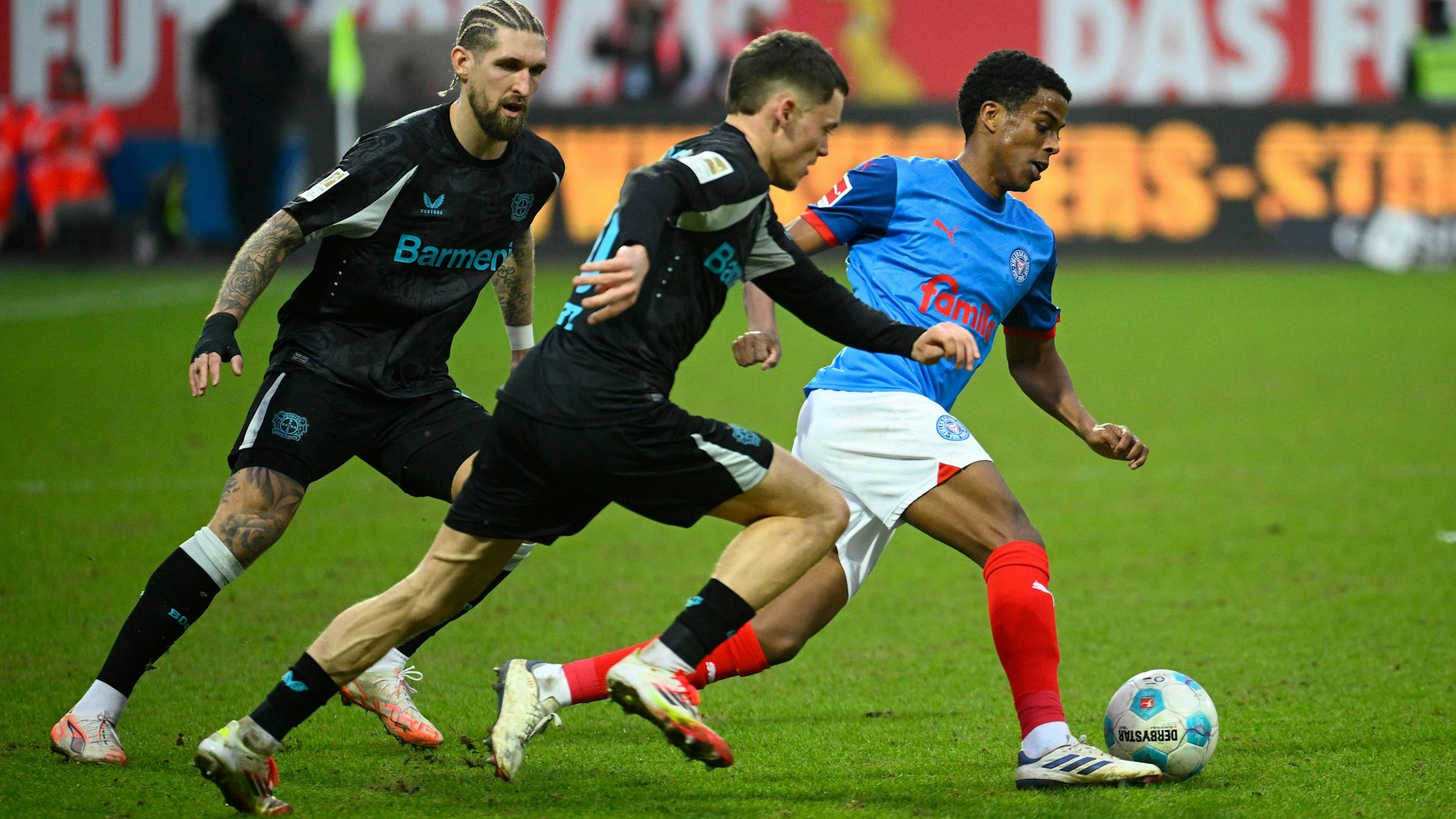 Kiels Andu Kelati (r) setzt sich gegen Leverkusens Robert Andrich (l) und Florian Wirtz durch.