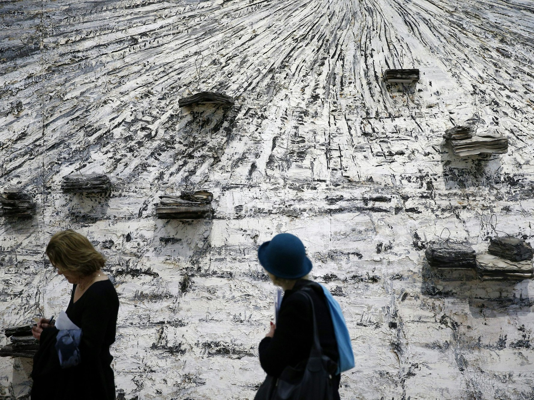 Zwei Besucherinnen stehen vor einem grauen, mit Büchern verzierten Gemälde.
