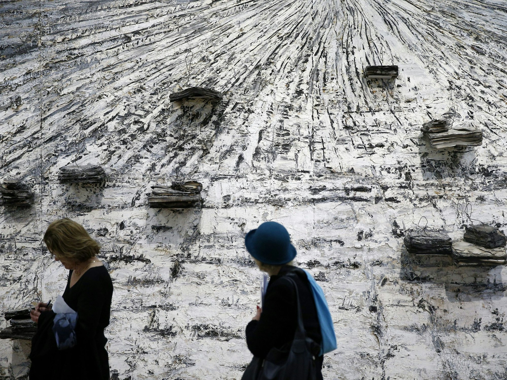 Zwei Besucherinnen stehen vor einem grauen, mit Büchern verzierten Gemälde.