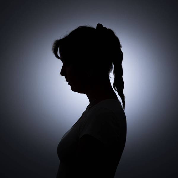 Die Silhouette einer jungen Frau zeichnet sich vor einer weissen Wand ab.