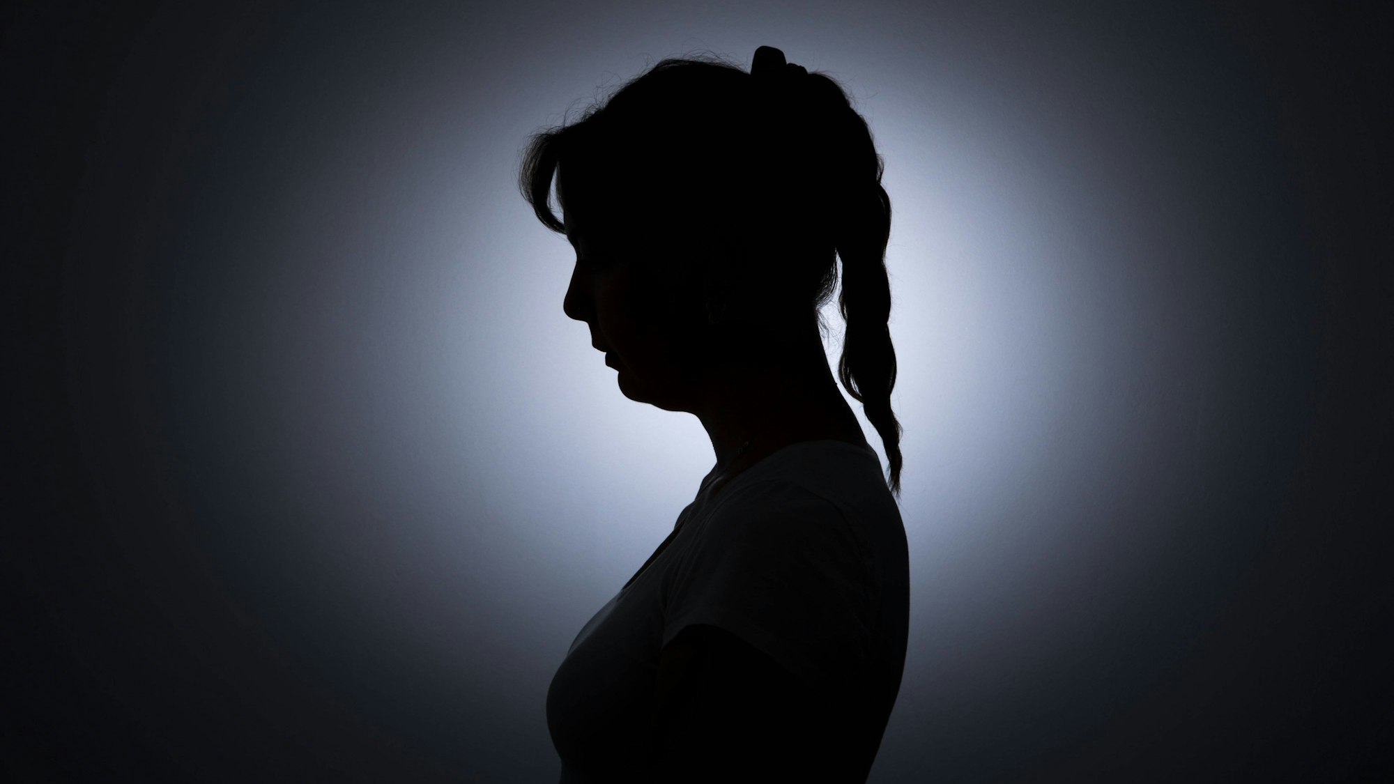 Die Silhouette einer jungen Frau zeichnet sich vor einer weissen Wand ab.