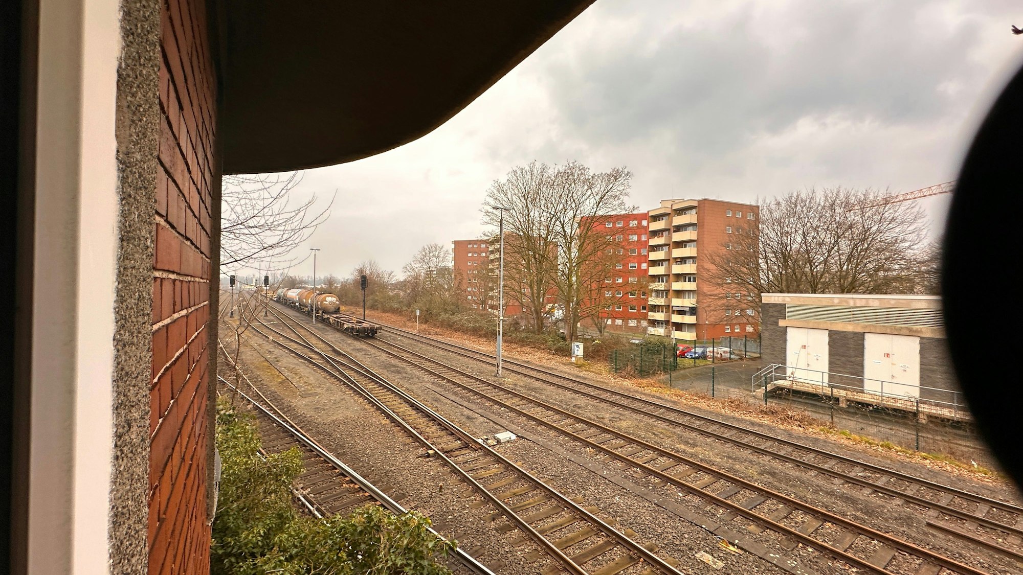 Aus einem Turm heraus fotografiert, sind Gleise und dahinter liegende Wohnblocks zu sehen.