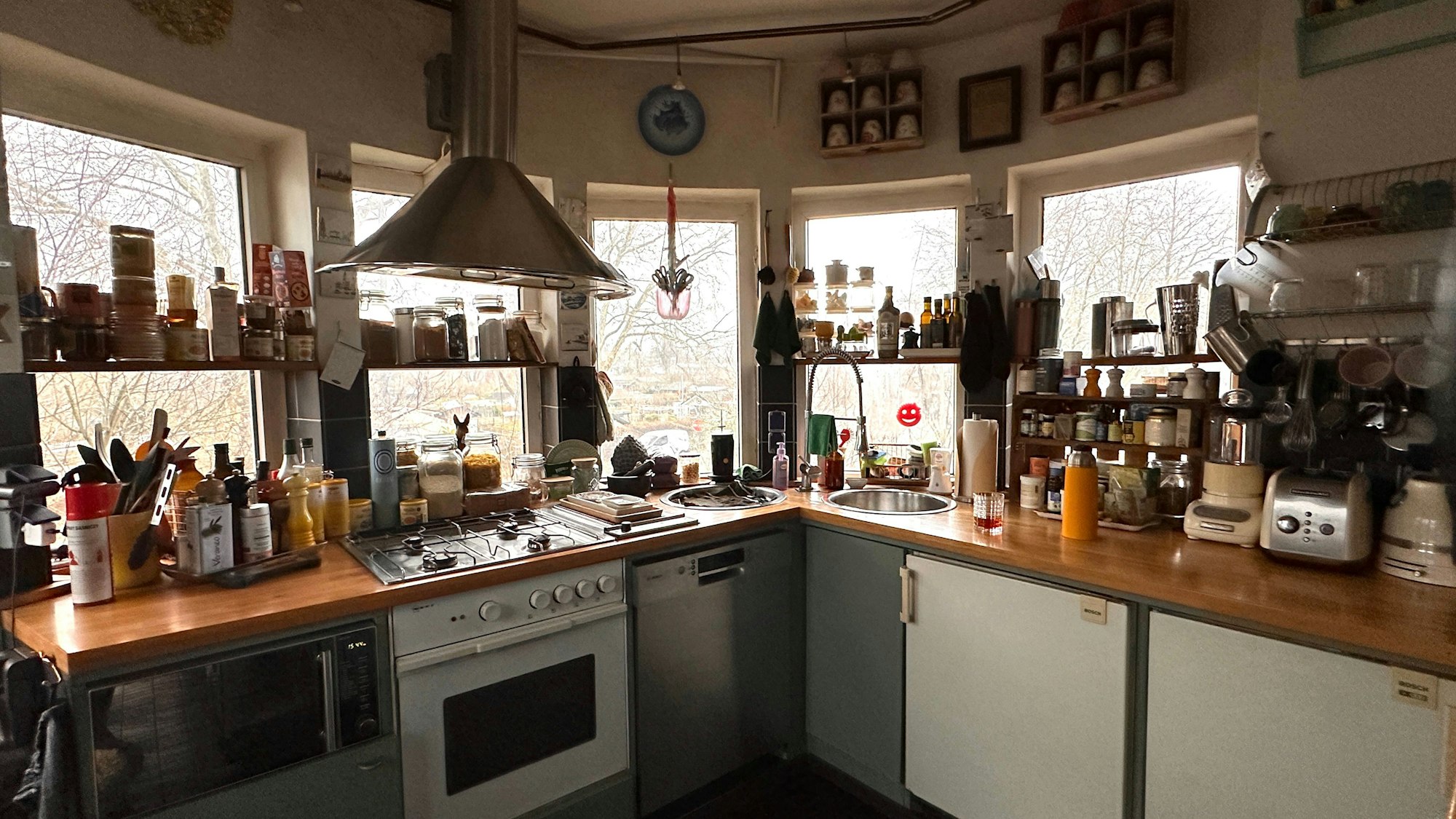 Blick in die Küche: Die Küchenzeile geht über Eck, vor den Fenstern sind Regale mit Gewürzen.