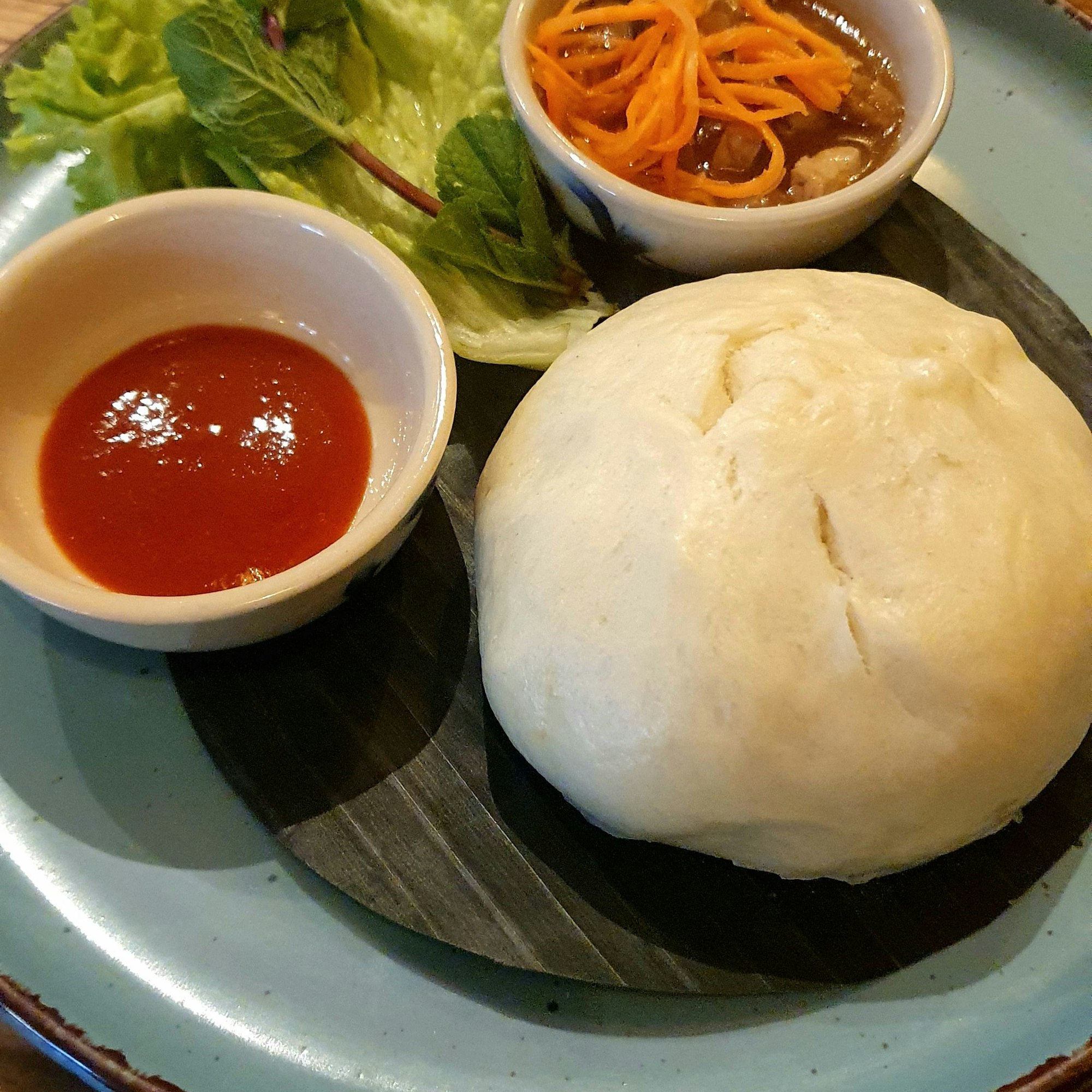 Ein Teller mit weißem fluffigen Kloß ist zu sehen, drumrum 2 Schälchen mit Beilagen und etwas Salat.