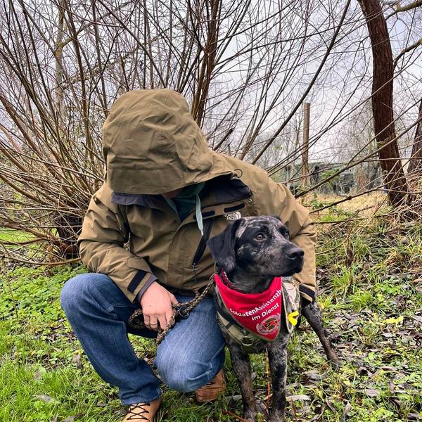 Das Foto zeigt einen Mann mit heruntergezogener Kapuze und einen Hund.