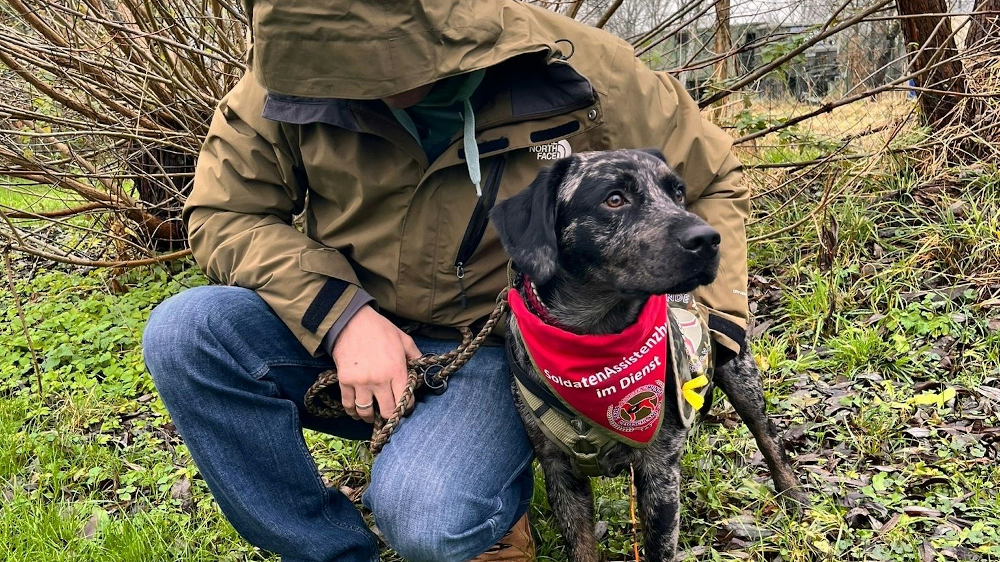Das Foto zeigt einen Mann mit heruntergezogener Kapuze und einen Hund.