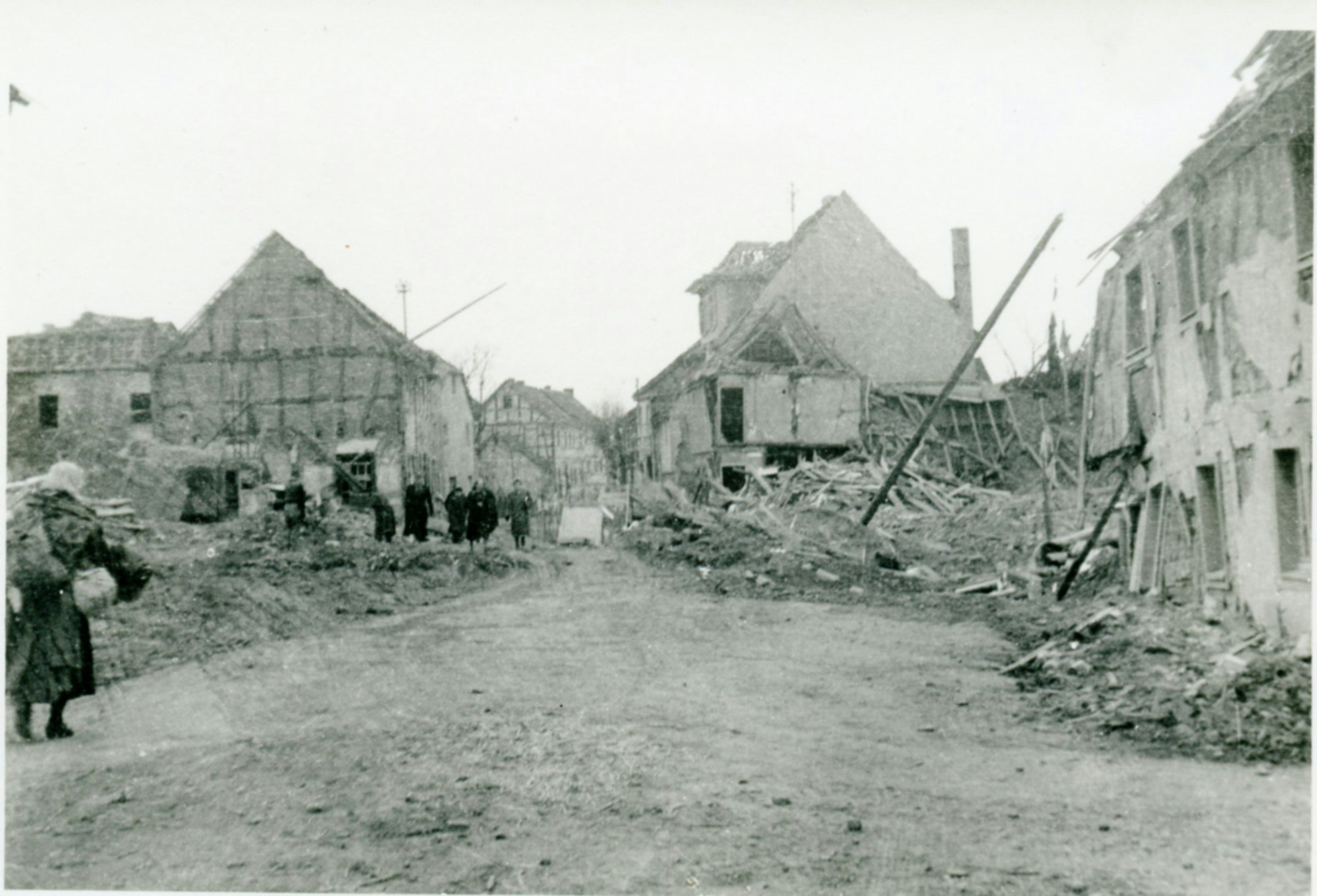 Bild von einer Straße mit zerstörten Häusern mit einigen Menschen.