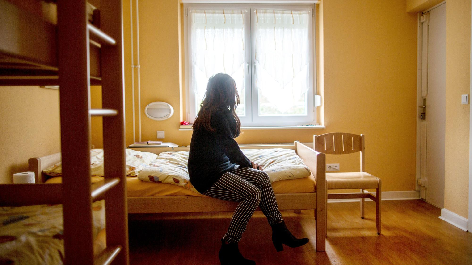 Eine Frau sitzt im Frauenhaus auf einem Bett. Das Gleichstellungsministerium in NRW will den Schutz von Frauen gegen Gewalt verbessern.