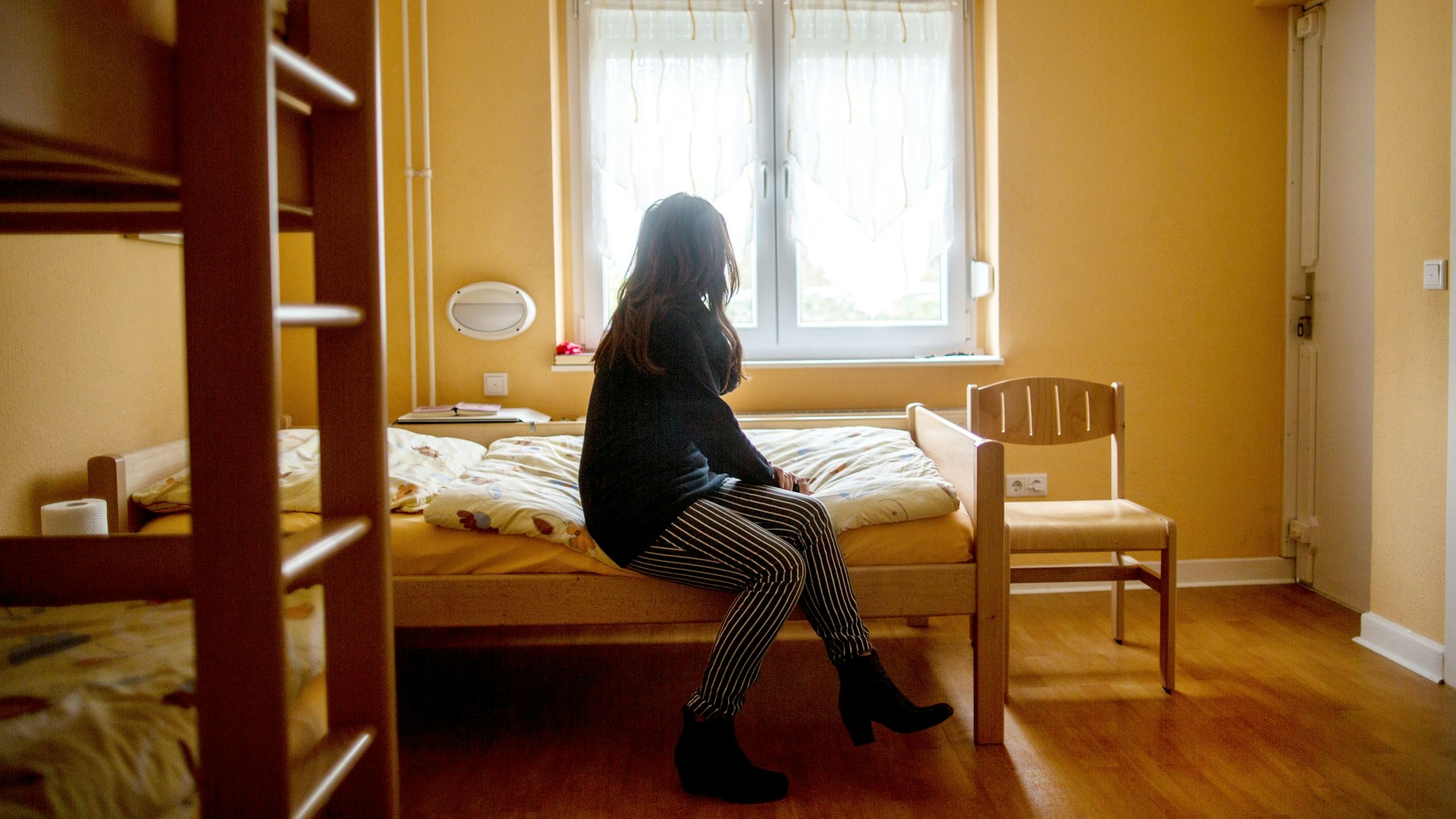 Eine Frau sitzt im Frauenhaus auf einem Bett.