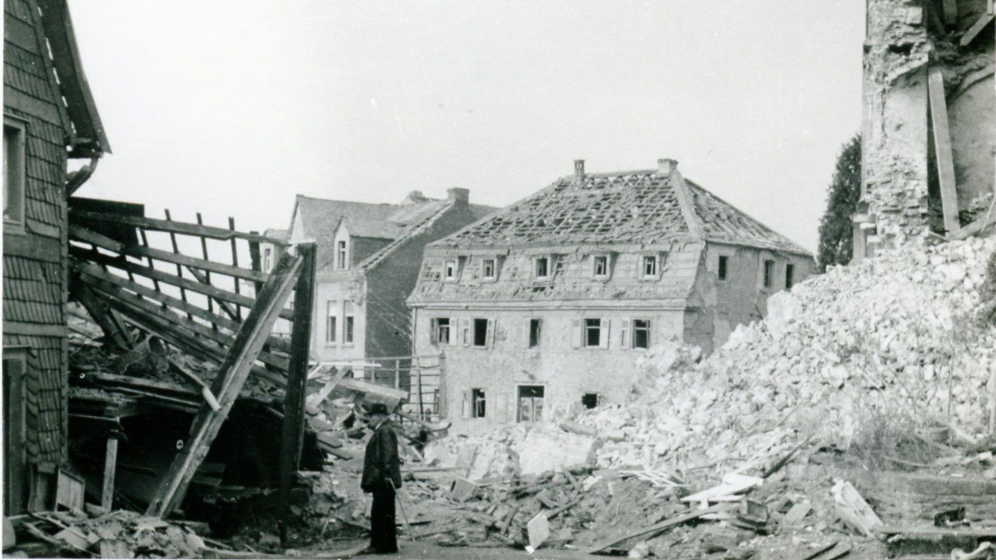 Zerbombte Häuser, Trümmer, ein Mann mit Stock, ein Haus ohne Dachpfannen.