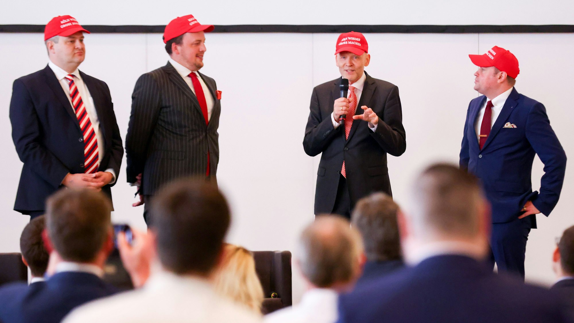 Stephan Boyens, Fraktionsvorsitzender der AFD Köln (am Mikrofon), und weitere AfD-Mitglieder mit roten Kappen im Gürzenich.