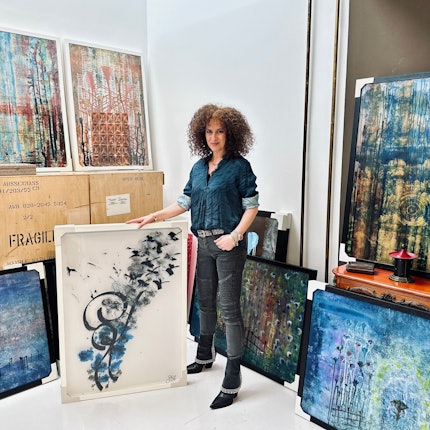 Eine Frau mit lockigem Haar steht inmitten von abstrakten großformatigen Bildern.