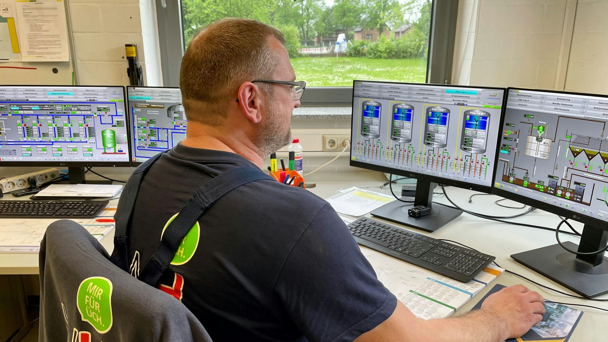 Das Foto zeigt einen Mann im Stadtwerke-T-Shirt vor einem Schreibtisch mit mehreren Computerbildschirmen.