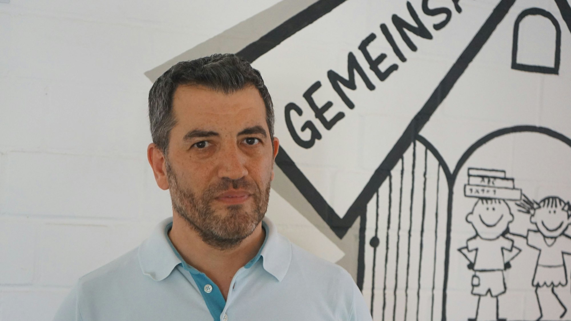 Auf dem Foto ist ein Mann in einem hellblauen Polohemd zu sehen. Er trägt einen Vollbart.