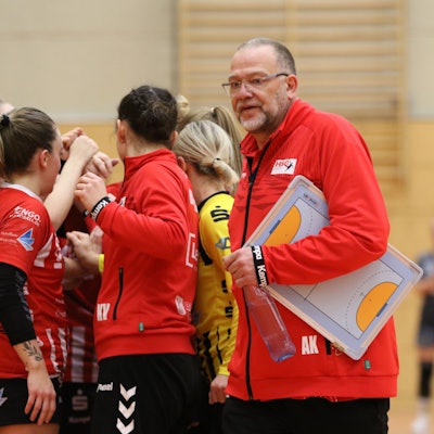 Andreas Kunzke hat ein Klemmbrett unter dem Arm und geht an seiner feiernden Mannschaft vorbei.