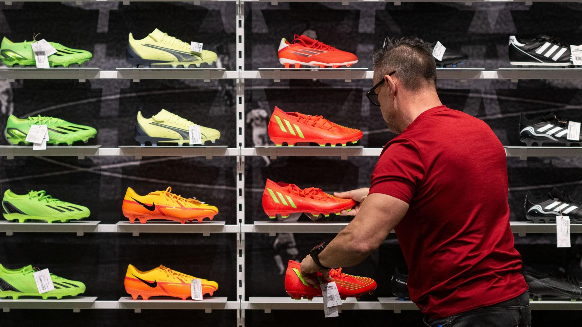 Ein Mitarbeiter Sportgeschäfts sortiert Fußballschuhe in einem Regal.