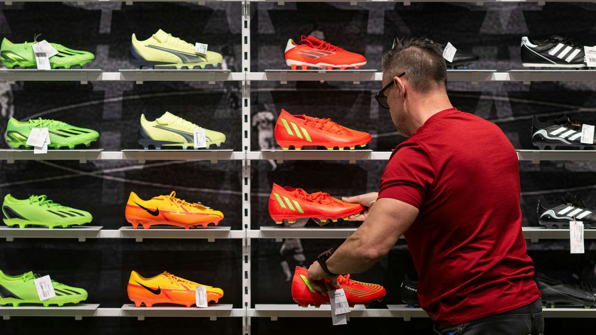 Ein Mitarbeiter Sportgeschäfts sortiert Fußballschuhe in einem Regal.