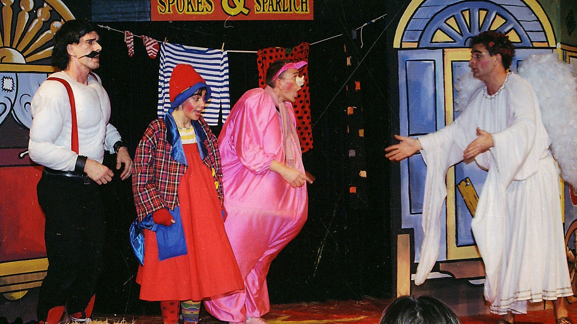 Auf der Bühne stehen ein als Engel verkleideter Schauspieler des Kölner Spielecircus, einer anderer im Schweinekostüm, eine als Clownin verkleidete Schauspielerin und Heiner Kötter als Muskelprotz.