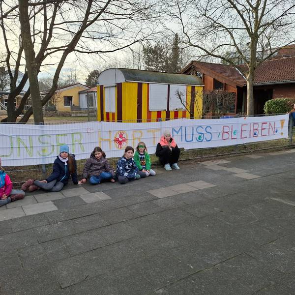 Auf dem Bild sind Kinder vor dem Hort vor einem selbst gemalten Transparent zu sehen.