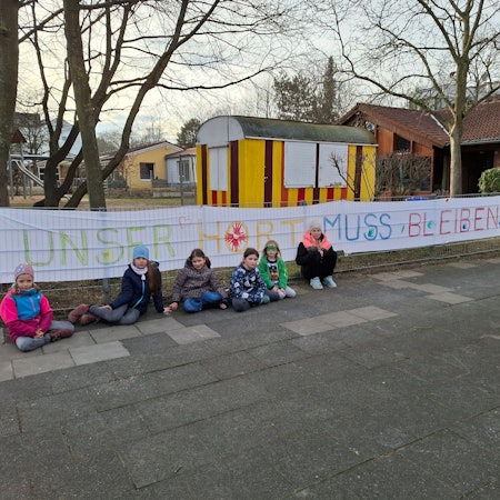 Auf dem Bild sind Kinder vor dem Hort vor einem selbst gemalten Transparent zu sehen.