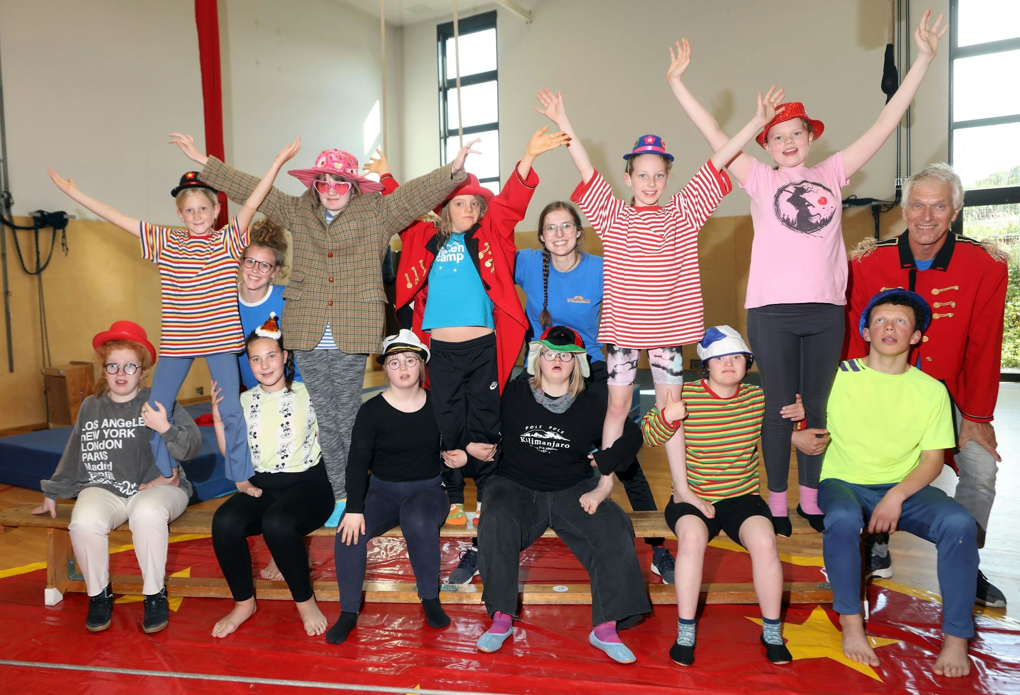 Kinder mit und ohne Behinderung sitzen verkleidet auf einer Bank in der Zirkus-Trainingshalle in Vogelsang.