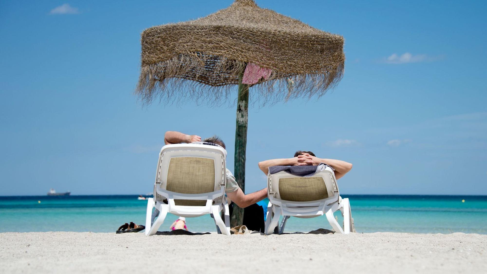 Zwei Menschen liegen auf Strandliegen an einem Strand und schauen auf das Meer.