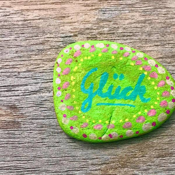 Auf einem Stein, der angemalt wurde, steht „Glück“.