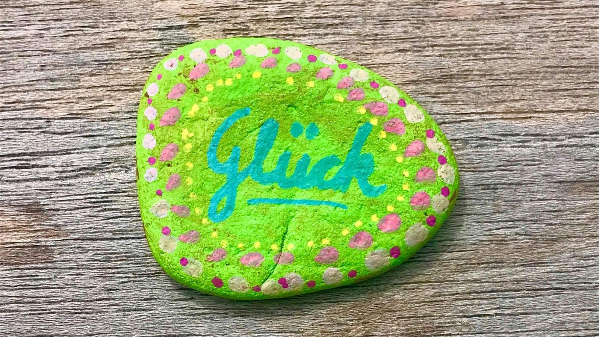 Auf einem Stein, der angemalt wurde, steht „Glück“.