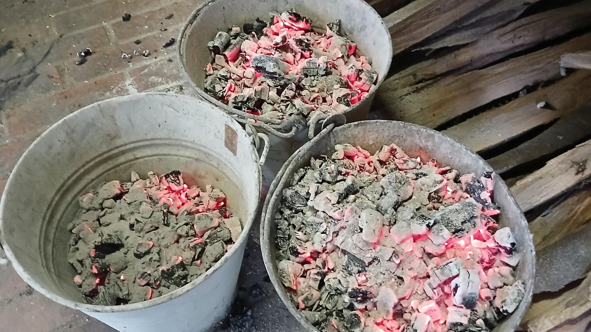 In drei feuerfesten Eimern sind glühende Hozstücke.
