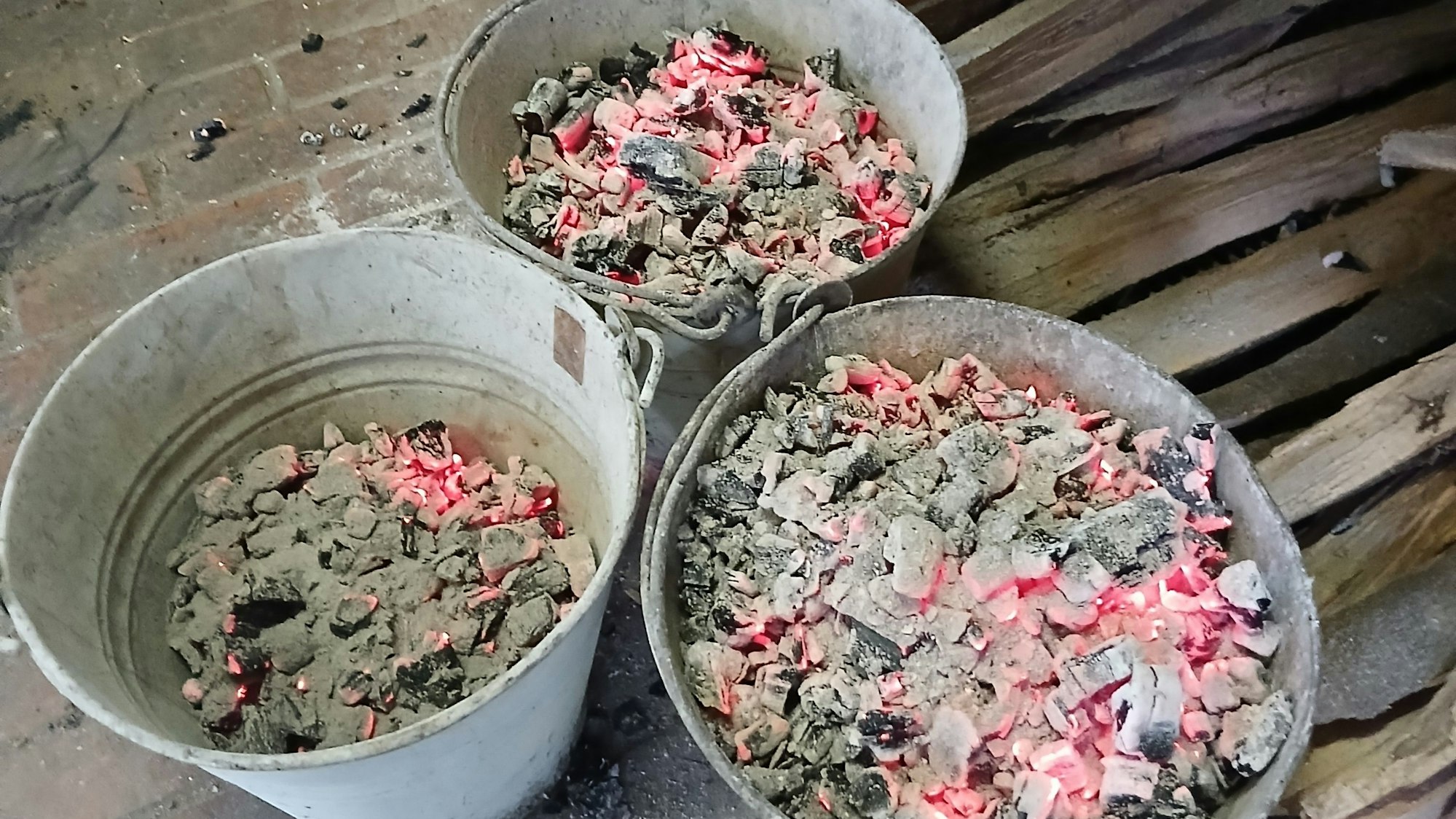 In drei feuerfesten Eimern sind glühende Hozstücke.