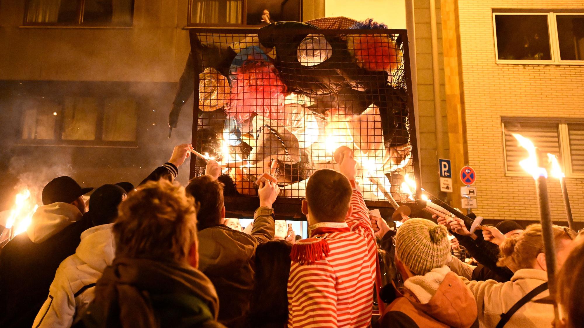 dpatopbilder - 05.03.2025, Nordrhein-Westfalen, Köln: Karnevalisten zündeln ihre «Nubbel» in dem Gefängniskäfig an. Der Nubbel, eine Puppe, wird traditionell in der Nacht zu Aschermittwoch verbrannt. Er büßt damit stellvertretend für die von den Menschen über Karneval begangenen Sünden. Foto: Roberto Pfeil/dpa +++ dpa-Bildfunk +++