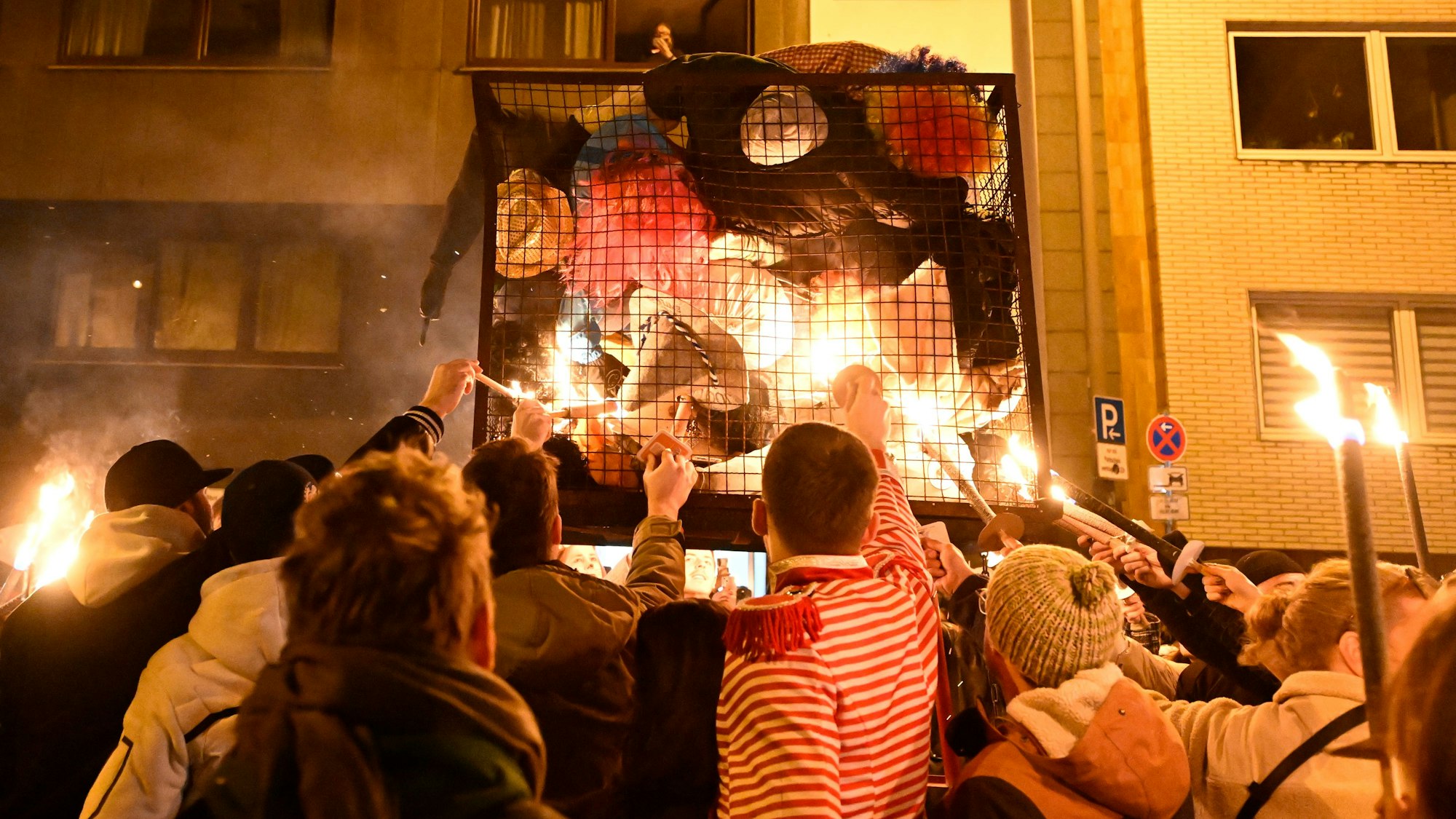 dpatopbilder - 05.03.2025, Nordrhein-Westfalen, Köln: Karnevalisten zündeln ihre «Nubbel» in dem Gefängniskäfig an. Der Nubbel, eine Puppe, wird traditionell in der Nacht zu Aschermittwoch verbrannt. Er büßt damit stellvertretend für die von den Menschen über Karneval begangenen Sünden. Foto: Roberto Pfeil/dpa +++ dpa-Bildfunk +++