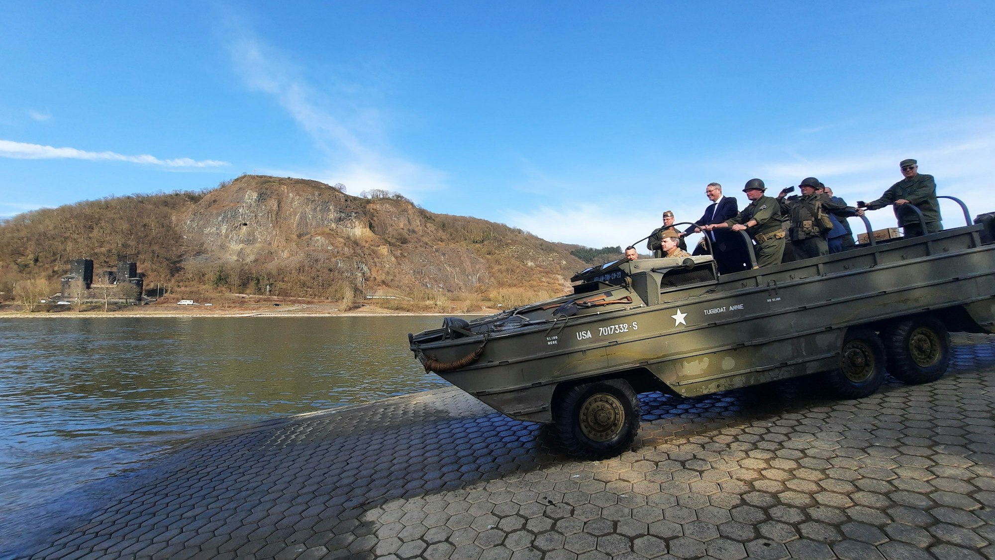Ein historisches Militärfahrzeug fährt über eine Rampe auf den Rhein zu.