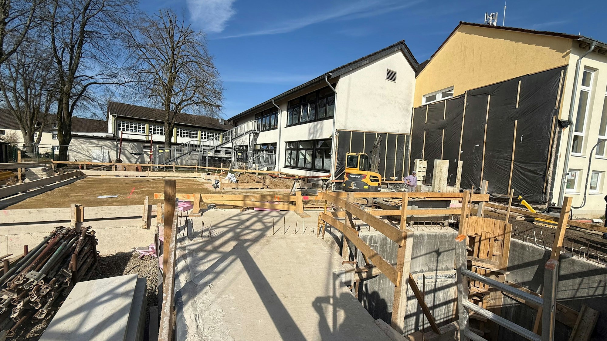 Eine Baustelle, im Hintergrund steht ein kleines Schulgebäüde.