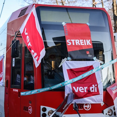 Eine mit Streik-Plakaten beklebte Straßenbahn der Kölner Verkehrs-Betriebe (KVB) steht vor dem Bahndepot. (Archivbild)