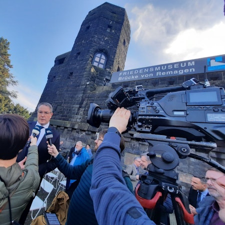 Journalisten interviewen vor den Türmen der Remagener Brücke den Ministerpräsidenten von Rheinland-Pfalz.