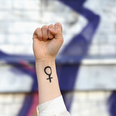 ILLUSTRATION - 07.03.2025, Sachsen, Leipzig: Eine Frau hebt ihre Faust in die Höhe. Auf ihrem Arm ist das Venussymbol zu sehen, das für das weibliche Geschlecht und Frauenrechte steht. Am ersten Frauentag kämpften die Frauen für ihr Wahlrecht. Auch in heutiger Zeit stehen Themen wie Gleichberechtigung, Frieden und Abrüstung im Vordergrund. Foto: Elisa Schu/dpa +++ dpa-Bildfunk +++