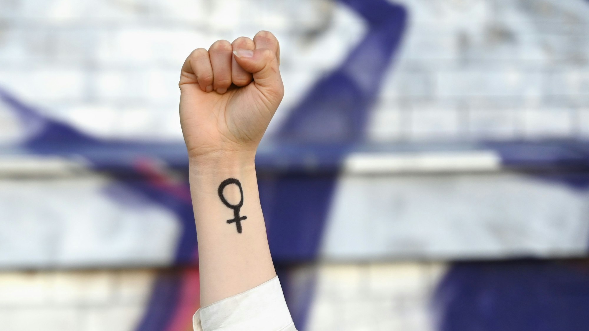 ILLUSTRATION - 07.03.2025, Sachsen, Leipzig: Eine Frau hebt ihre Faust in die Höhe. Auf ihrem Arm ist das Venussymbol zu sehen, das für das weibliche Geschlecht und Frauenrechte steht. Am ersten Frauentag kämpften die Frauen für ihr Wahlrecht. Auch in heutiger Zeit stehen Themen wie Gleichberechtigung, Frieden und Abrüstung im Vordergrund. Foto: Elisa Schu/dpa +++ dpa-Bildfunk +++