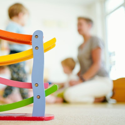 Eine Erzieherin spielt in einer Kindertagesstätte hinter einer Rollbahn mit Kindern.