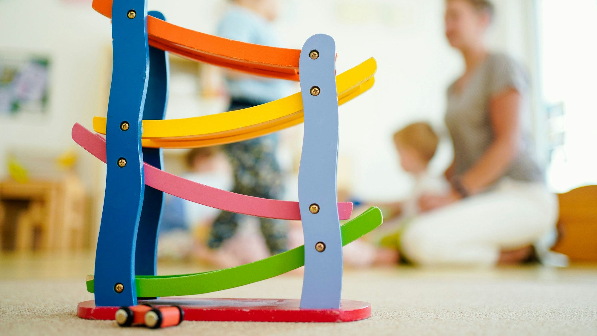 Eine Erzieherin spielt in einer Kindertagesstätte hinter einer Rollbahn mit Kindern.