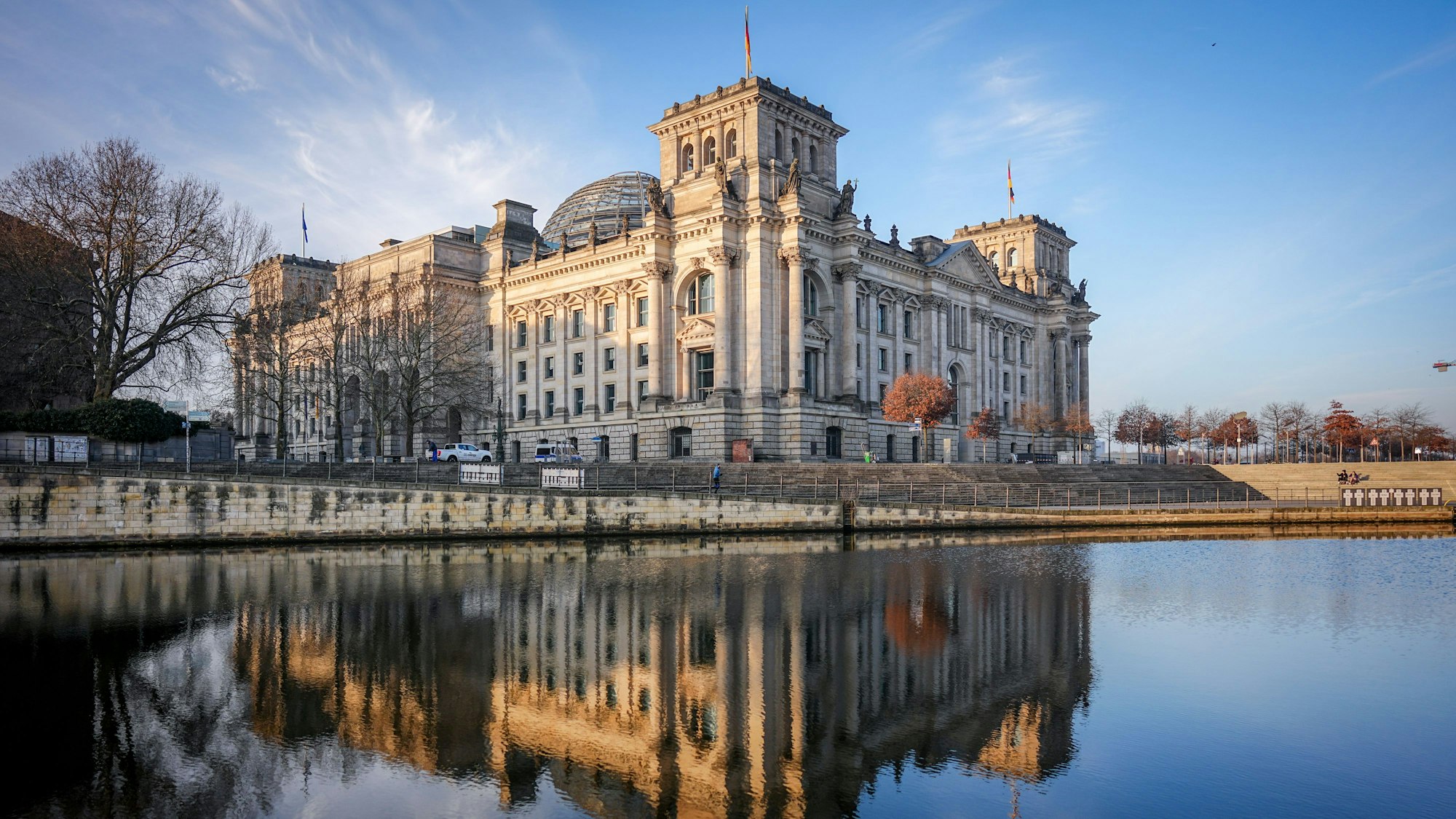 Das Reichstagsgebäude spiegelt sich in der Morgensonne in der Spree. Die Unionsparteien und die SPD verhandeln weiter über eine Regierungsbildung.