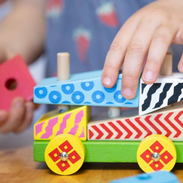 Man sieht eine Kinderhand, die ein Auto aus Holzbausteinen schiebt.