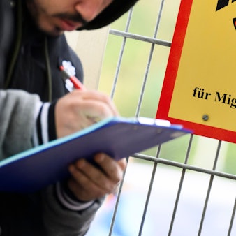 Ein Mann füllt ein Formular aus neben einem Schild vom Bundesamt für Migration und Flüchtlinge an der Landesaufnahmebehörde Niedersachsen am Standort Braunschweig.